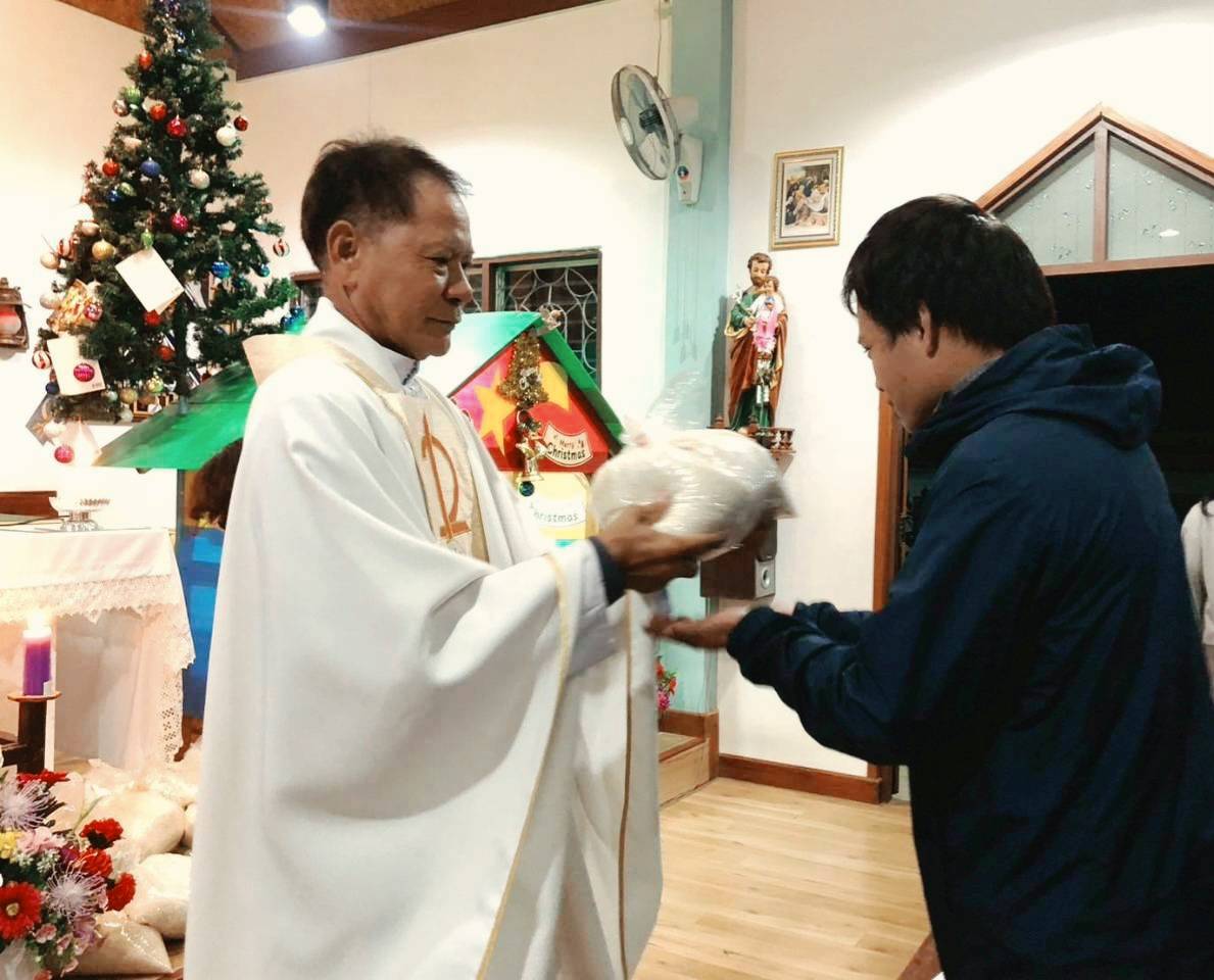 A priest handing a bag of rice to a parishioner at Christmas